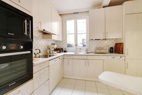La cuisine est équipée de placards blancs et d'un four micro-ondes noir. dans l'établissement Séjour au pied de la tour Eiffel, à Paris