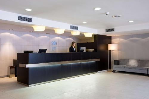 a woman standing at a reception desk in a lobby at NH Lleida Pirineos in Lleida