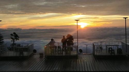 a group of people standing on top of a pier with the sunset at สเตชั่นภูทับเบิก-บ้านดาดฟ้าทะเลหมอก in Ban Tha Kok Hai