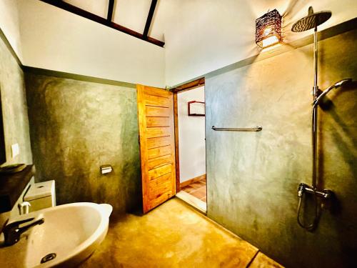 a bathroom with a sink and a shower and a door at Riva del Sole Guest House in Arugam Bay