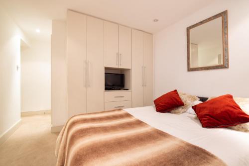 een slaapkamer met een bed met rode kussens en een spiegel bij Niru Experience Hidden Gem in Chelsea in Londen
