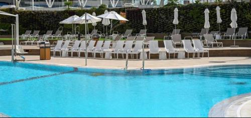 a swimming pool with white chairs and umbrellas at Beach Side- Ceasar Luxury Amazing Pool Eilat in Eilat