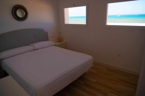 a bedroom with a white bed and two windows at Hostal Paraiso del Mar in Torre del Mar