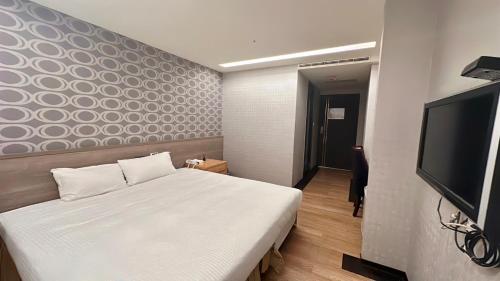 um quarto com uma cama branca e uma televisão de ecrã plano em Crystal City Hotel em Zhongli