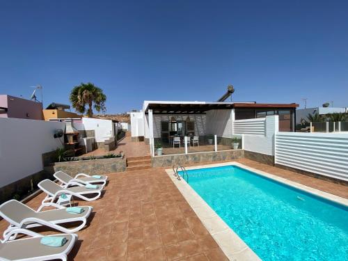 a swimming pool with lounge chairs next to a house at Casa Blanca Caleta - Golf & Sea Views - private heated Saltwater Pool - BBQ - Aircondition" in Caleta De Fuste
