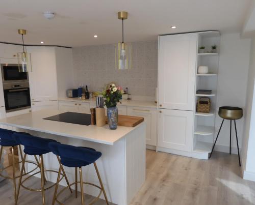 a kitchen with white cabinets and blue bar stools at Fabulous Ground Floor Apt Adjacent to Beach in Rhosneigr