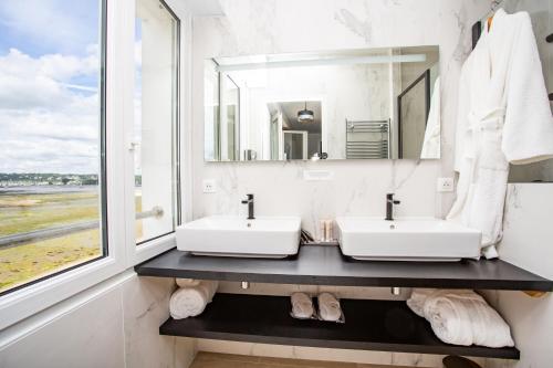La salle de bains est pourvue de 2 lavabos et d'une grande fenêtre. dans l'établissement Logis Hôtel de la Pointe du Cap Coz, à Fouesnant
