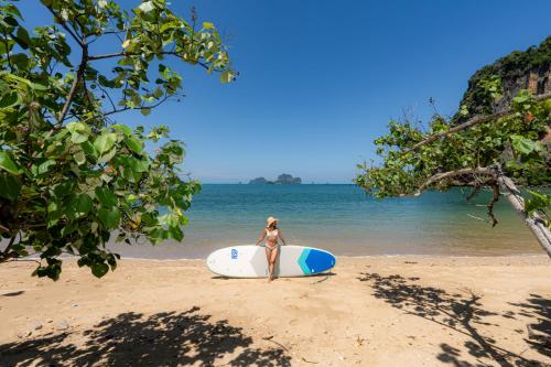 a woman in a bikini standing on a beach with a surfboard at Tinidee Hideaway Tonsai Beach Krabi - SHA Extra Plus in Tonsai Beach
