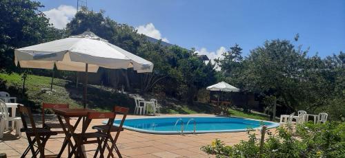 uma piscina com um guarda-sol e cadeiras e uma mesa com um guarda-sol em Pousada Aldeia Banzaê em Imbassaí