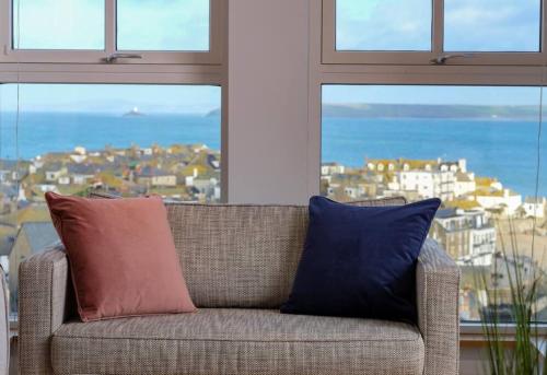 a couch with two pillows in a room with windows at Luxurious apartment, 180° beach views & parking in St Ives