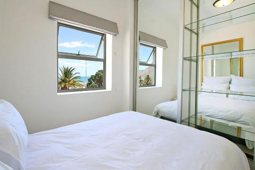 a white bedroom with two beds and two windows at Brighton Court in Campsbay on the beach. in Cape Town