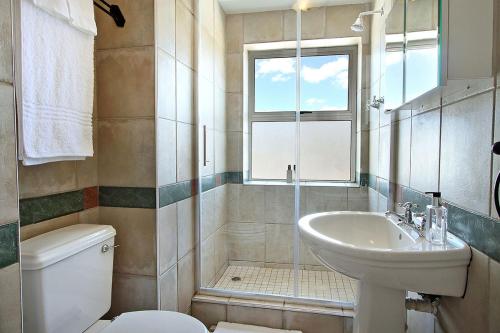 a bathroom with a sink and a toilet and a window at Brighton Court in Campsbay on the beach. in Cape Town