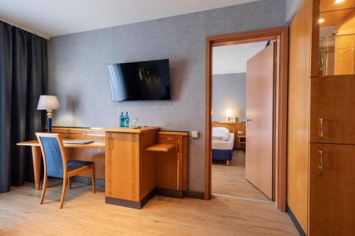 a hotel room with a desk and a television on the wall at ACHAT Hotel Magdeburg in Magdeburg