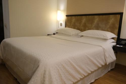 a large white bed with white sheets and pillows at Four Points by Sheraton Vadodara in Vadodara