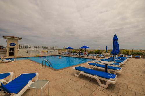 a swimming pool with lounge chairs and blue umbrellas at The White Sands Resort and Spa in Point Pleasant Beach