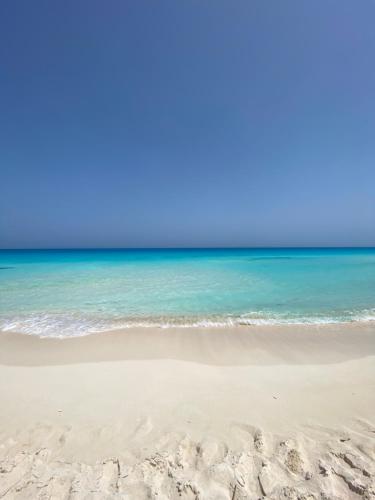 a sandy beach with the ocean in the background at 50% Off. 2BR , 2BR Ground floor with pool view, private beach access, security 24/7 شاليه ٢ غرفه ، ٢ حمام ف الدور الارضي قدام جنينه و حمام السباحه مباشره ، شاطيء خاص بالقرية و أمن ٢٤ ساعه و مسجد خاص in Dawwār Muḩammad Abū Shanab