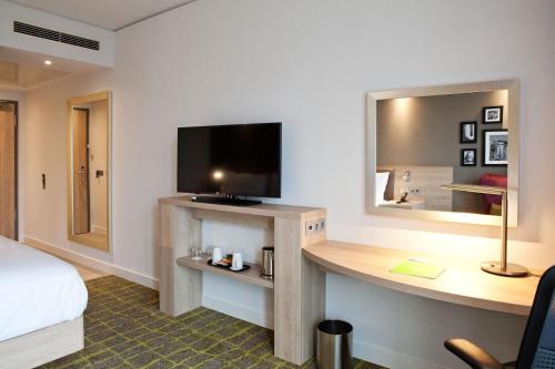 a hotel room with a bed and a desk with a television at Hampton By Hilton Dortmund Phoenix See in Dortmund