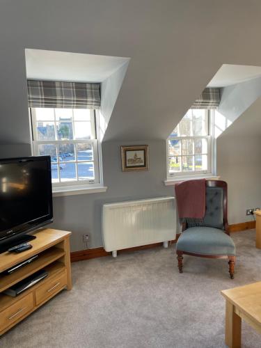 a living room with a tv and a chair and windows at The Town House in Dornoch