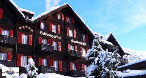 a building with red shuttered windows and a snow covered tree at Romantik Hotel Schweizerhof in Grindelwald