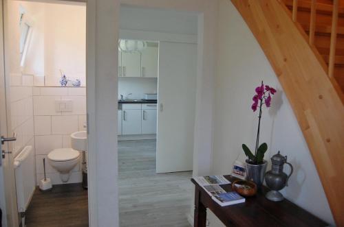 a bathroom with a toilet and a table with a flower on it at Hus Oldewurth in Oldenswort