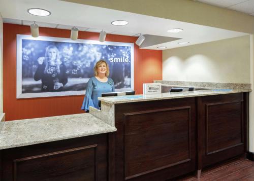 a woman standing in front of a screen in a waiting room at Hampton Inn Dallas Irving Las Colinas in Irving