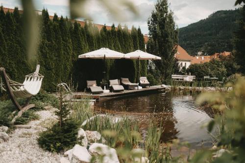 - un groupe de chaises et de parasols à côté d'un étang dans l'établissement Hotel Rosenhof Murau, à Murau