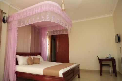 Jatheo Hotel Rwentondo في Mbarara: غرفة نوم مع سرير مظلة مع ستائر وردية