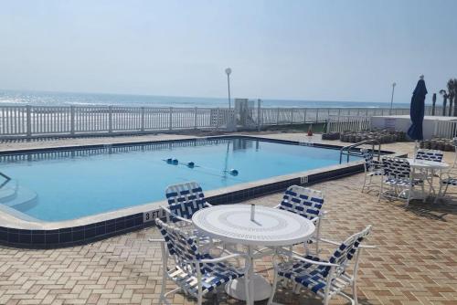 a swimming pool with a table and chairs and the ocean at Aliki Atrium Beachfront Condo in Ormond Beach