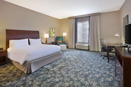 um grande quarto de hotel com uma cama e uma secretária em Hilton Garden Inn Detroit/Novi em Novi