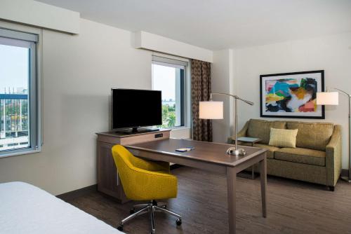 a hotel room with a desk with a tv and a couch at Hampton Inn & Suites Miami Wynwood Design District, FL in Miami