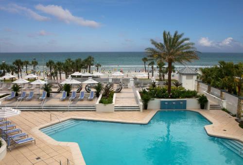 ein Schwimmbad mit Strand im Hintergrund in der Unterkunft Hilton Daytona Beach Resort in Daytona Beach