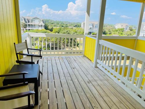a balcony with two chairs and a yellow house at The Skipper condo in Holden Beach