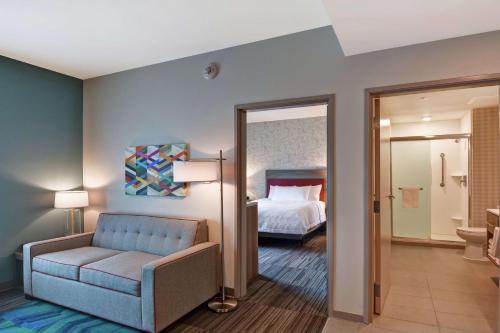 a hotel room with a bed and a blue couch at Home2 Suites By Hilton Daytona Beach Speedway in Daytona Beach