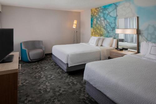 a hotel room with two beds and a chair at Courtyard by Marriott Daytona Beach Speedway/Airport in Daytona Beach