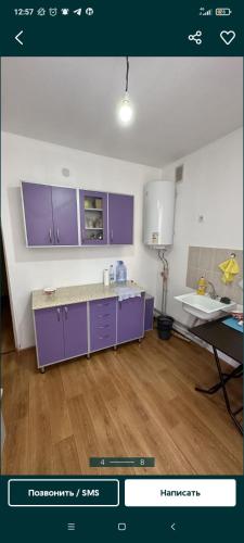 a kitchen with purple cabinets and a wooden floor at Квартира in Tridtsatʼ Let Kazakhstana