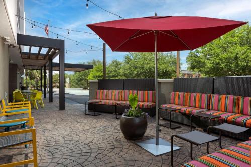 une terrasse avec un parasol rouge, des bancs et des tables dans l'établissement Home2 Suites by Hilton Charleston Airport Convention Center, SC, à Charleston