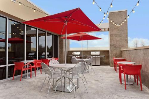 un patio con mesas, sillas y sombrillas rojas en Home2 Suites by Hilton Baltimore/Aberdeen MD, en Aberdeen