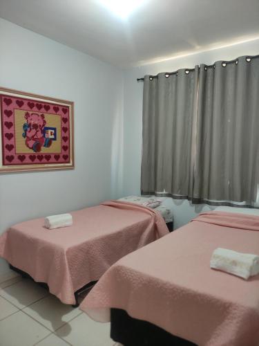 Zimmer mit 2 Betten mit rosa Bettwäsche und einem Bild in der Unterkunft Apto Recanto Aconchego (B-E 32) in Rio Verde