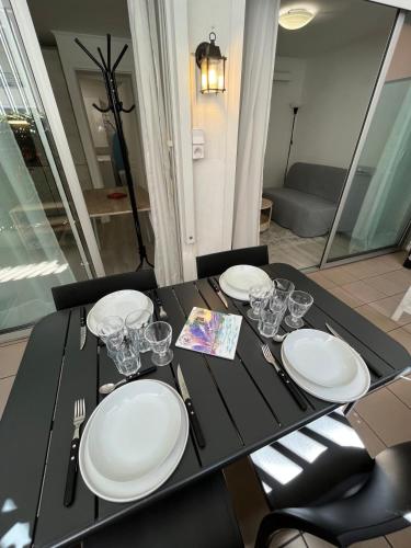 una mesa negra con platos blancos y gafas. en Apartment cosy with terrace 200m from the sandy beaches wifi, en Juan-les-Pins