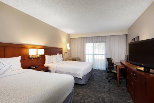 a hotel room with two beds and a flat screen tv at Courtyard by Marriott Dallas-Fort Worth/Bedford in Bedford