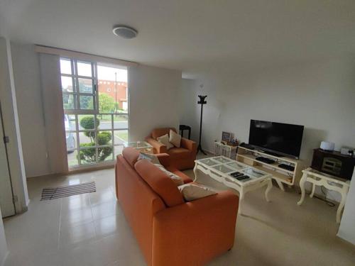 sala de estar con muebles de color naranja y TV de pantalla plana. en Agradable casa para descansar en Villas de Campo en Calimaya de Díaz González