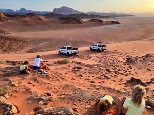 a group of people sitting in the desert with vehicles at Wadi Rum Aviva camp in Wadi Rum