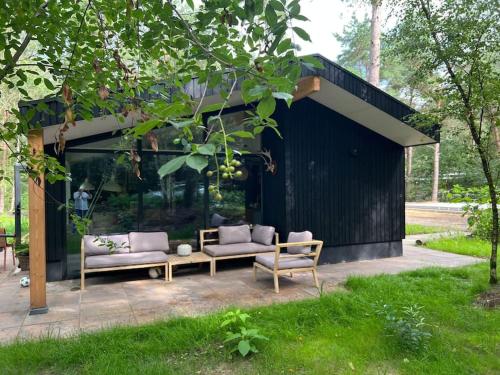 a black building with two couches and chairs in a yard at Heerlijk familiehuis in het bos in Giethmen