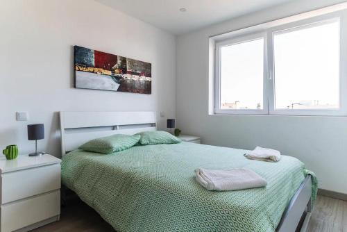 a white bedroom with a bed and two windows at Encantador Apartamento à frente da praia do Sunset in Figueira da Foz