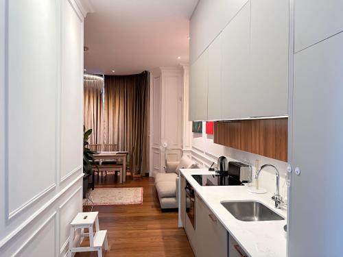 a white kitchen with a sink and a living room at Luxurious 2-Bedroom, 2-Bathroom Paddington Retreat with En-Suite TV Bed in London