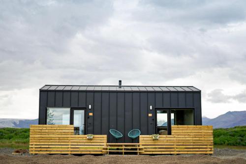 a black tiny house with two blue chairs at HH Gisting/Guesthouse in Hólmur