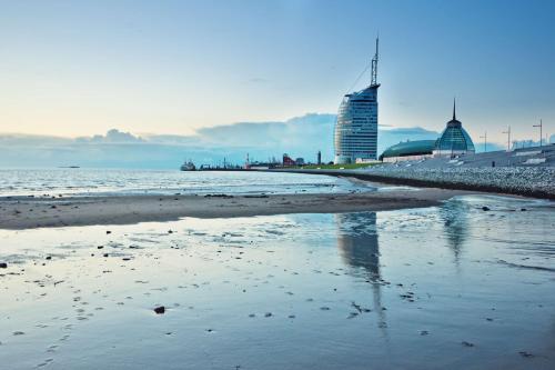 einen Strand mit Gebäuden im Hintergrund und dem Meer in der Unterkunft Atlantic Hotel Sail City in Bremerhaven