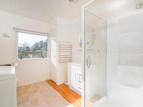 La salle de bains blanche est pourvue d'une douche et d'un lavabo. dans l'établissement Sunbathe Bach - Whitianga Holiday Home, à Whitianga