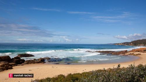 a beach with rocks and the ocean on a sunny day at The Gull Ocean views family home Bermagui in Bermagui