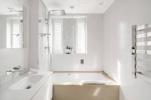 uma casa de banho branca com uma banheira e um lavatório em A South Bondi Family Hideout for Beach Aficionados em Sydney
